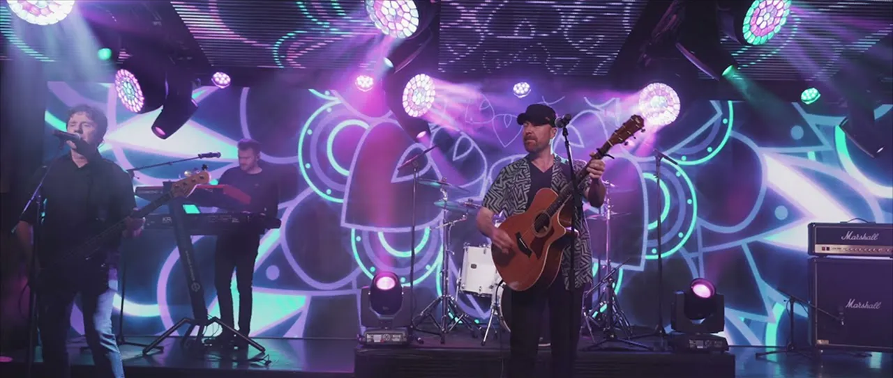 Band performing on stage with colorful neon abstract background and purple stage lights.